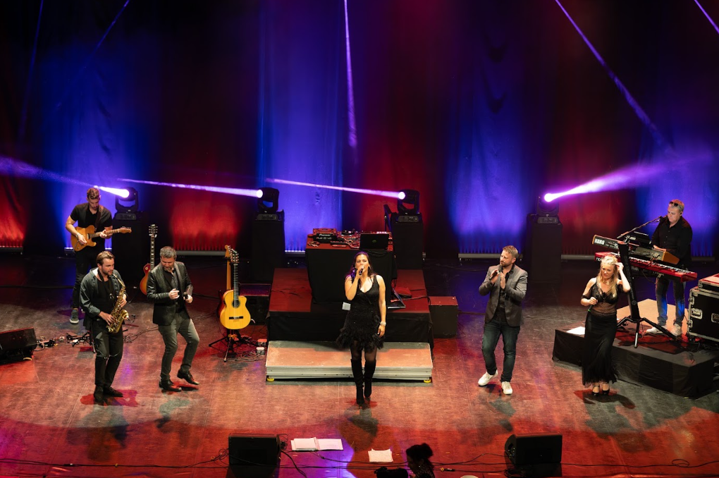 Vue large d'un groupe de sept musiciens sur scène