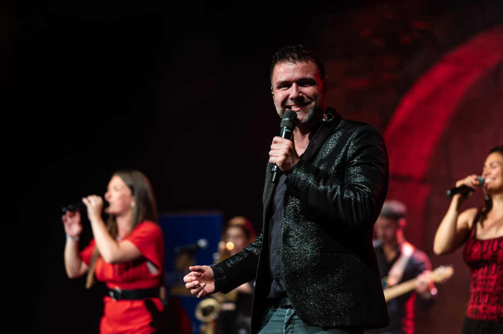 Chanteur souriant au micro devant son groupe