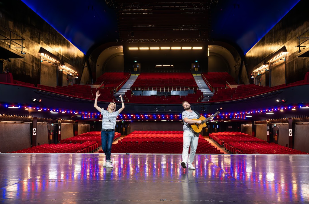 Deux artistes sur la scène d'une grande salle de spectacle vide